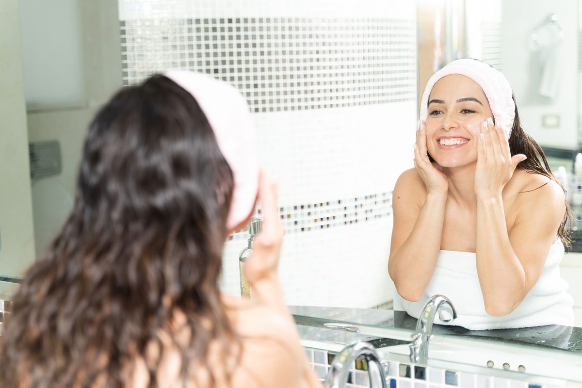 A woman is applying skincare and smiling in the bathroom
