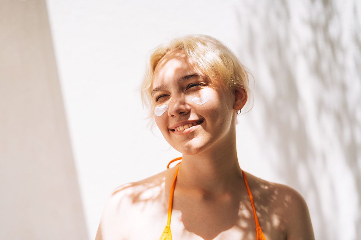 A girl with suncream on her face that has not been absorbed is smiling
