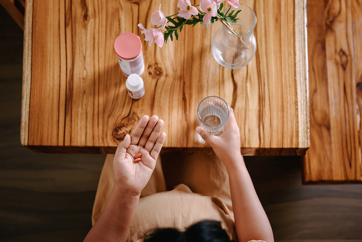 An overhead shot of female hands holding a glass of water and two orange tablets