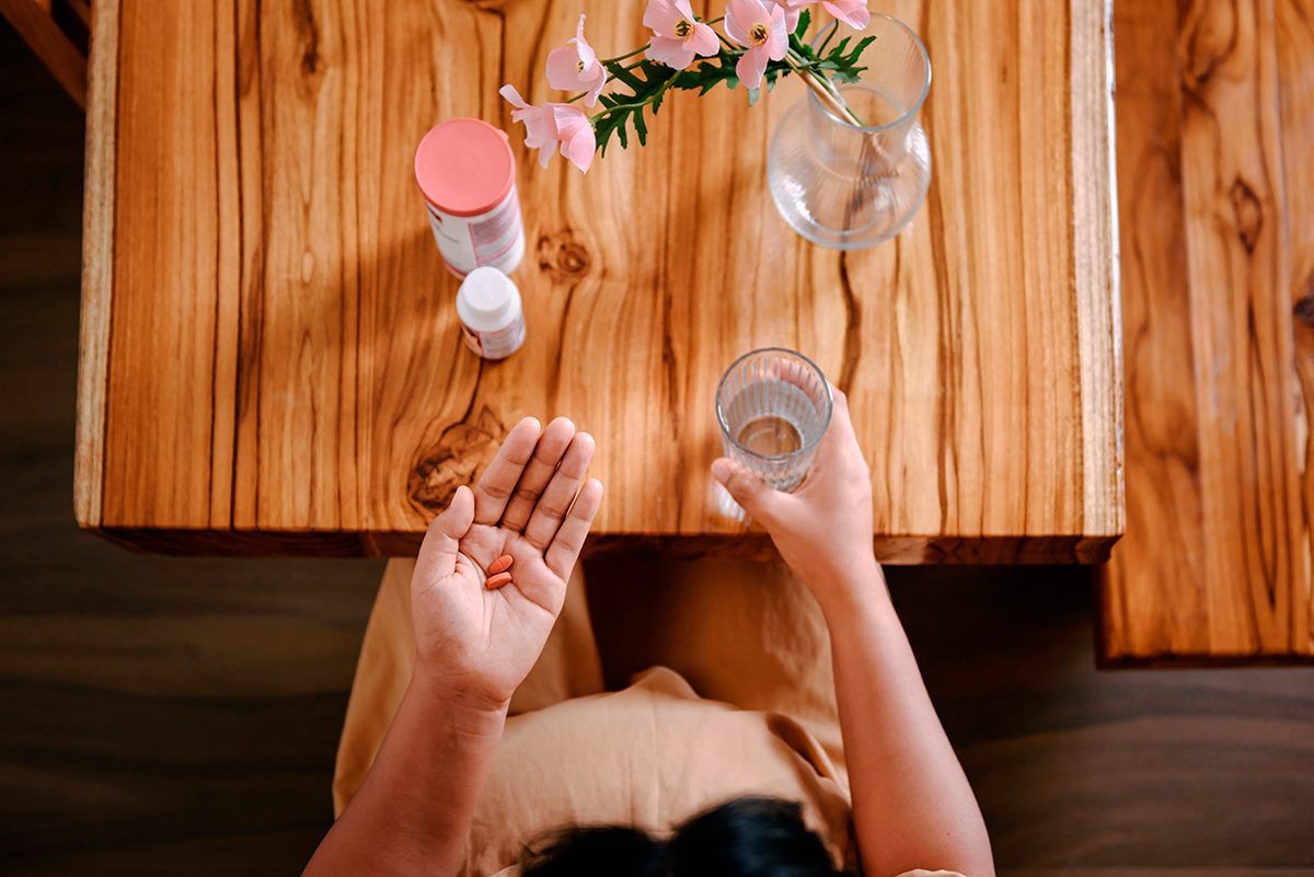 An overhead shot of female hands holding a glass of water and two orange tablets