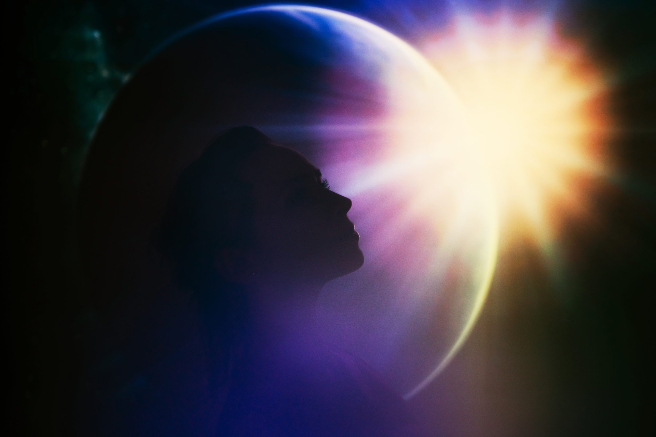 A silhouette of a woman’s profile set against a glowing planet and sunburst