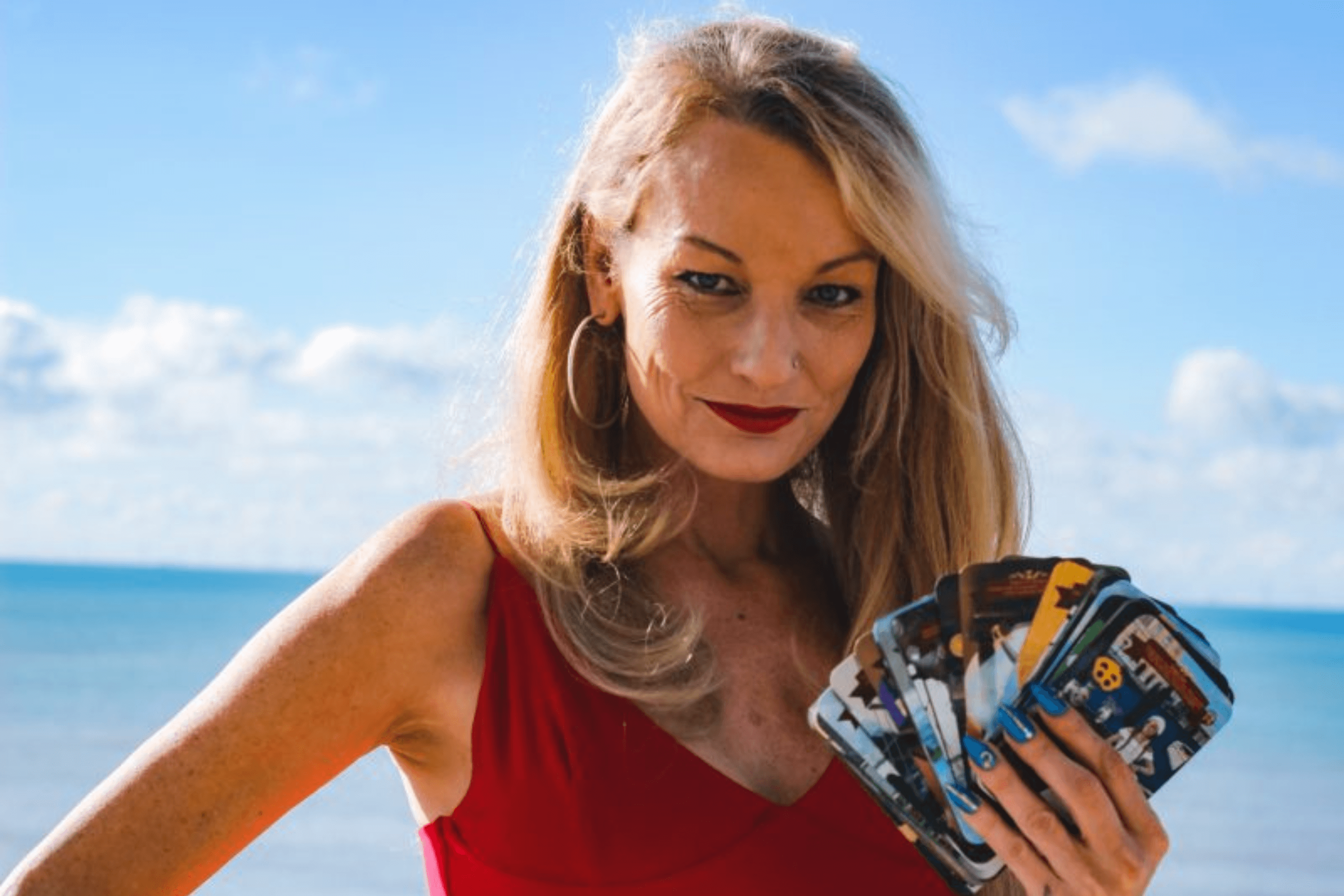 Woman in red bathing suit holds tarot cards on the beach