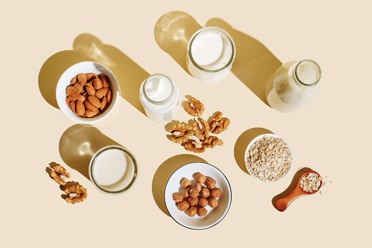 A selection of plant-based milks, nuts, and oats on a beige background