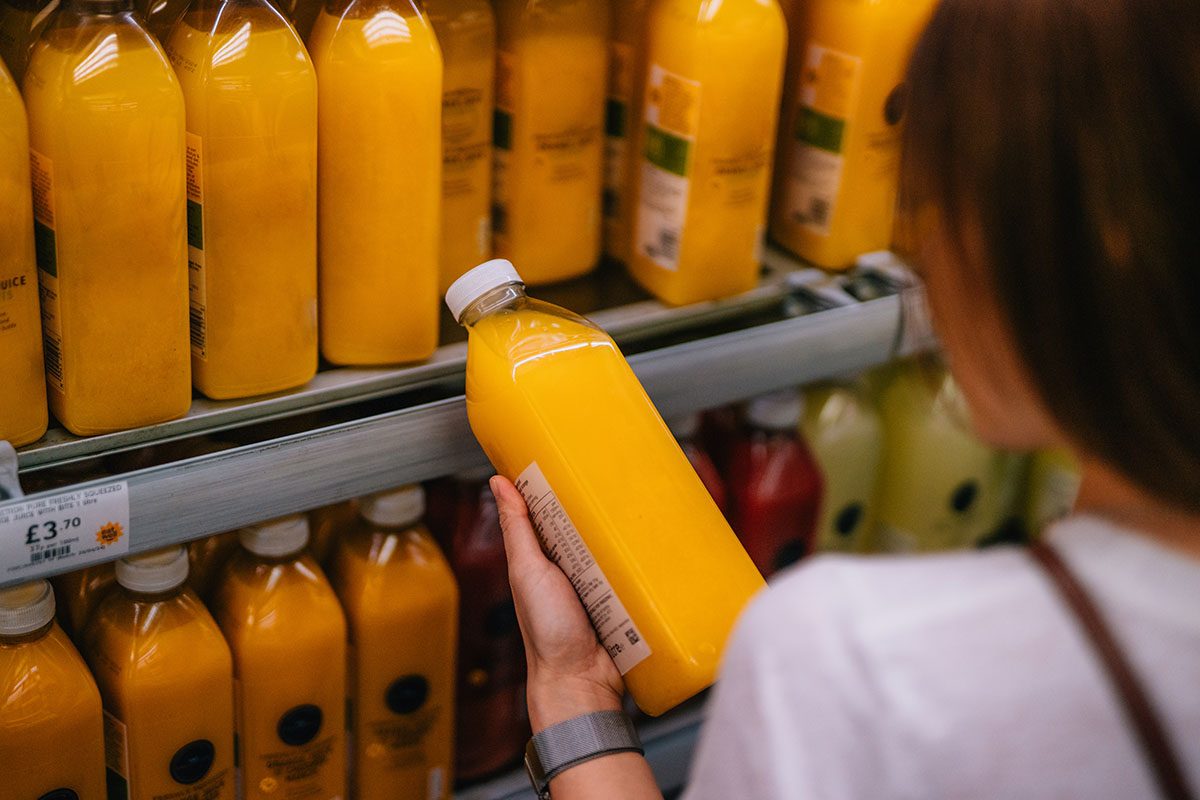 A woman picking up a bottle of fresh orange juice in a supermarket