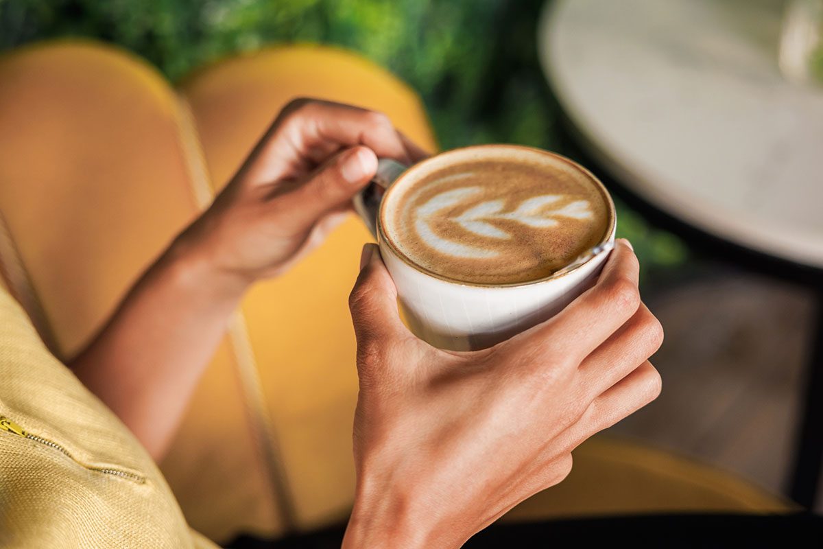 A close-up of a person's hands holding a latte featuring intricate latte art