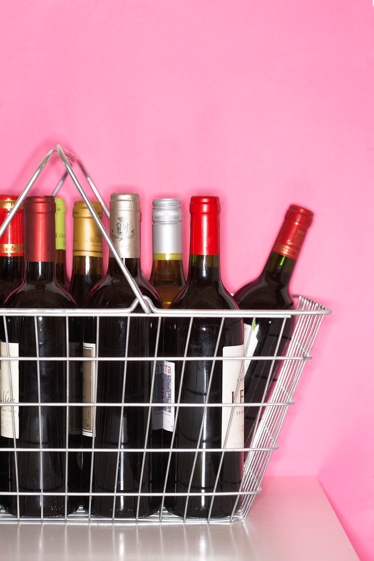 A basket containing bottles of red wine against a pink background