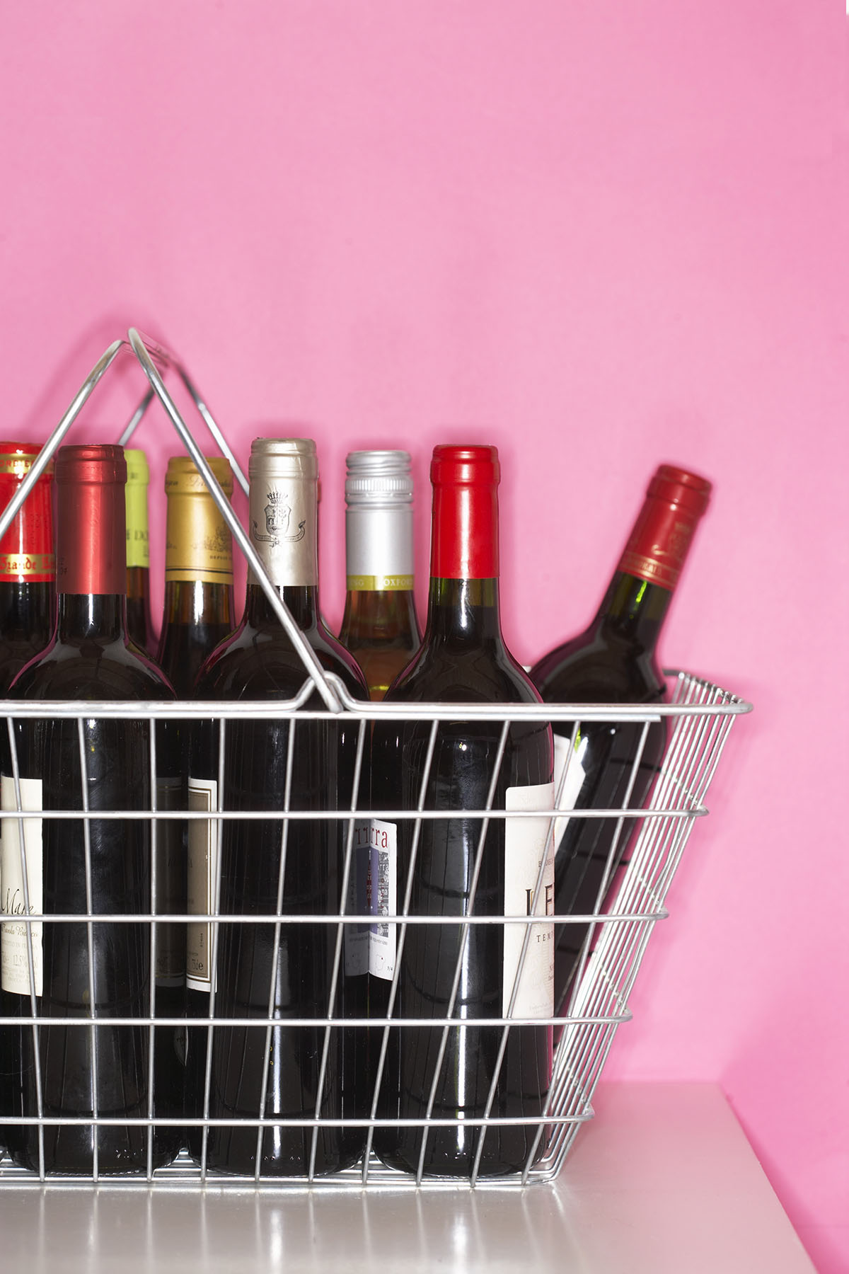 A basket containing bottles of red wine against a pink background