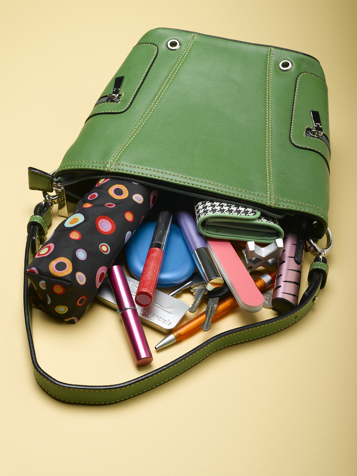A green handbag lays on a beige surface with the contents spilling out