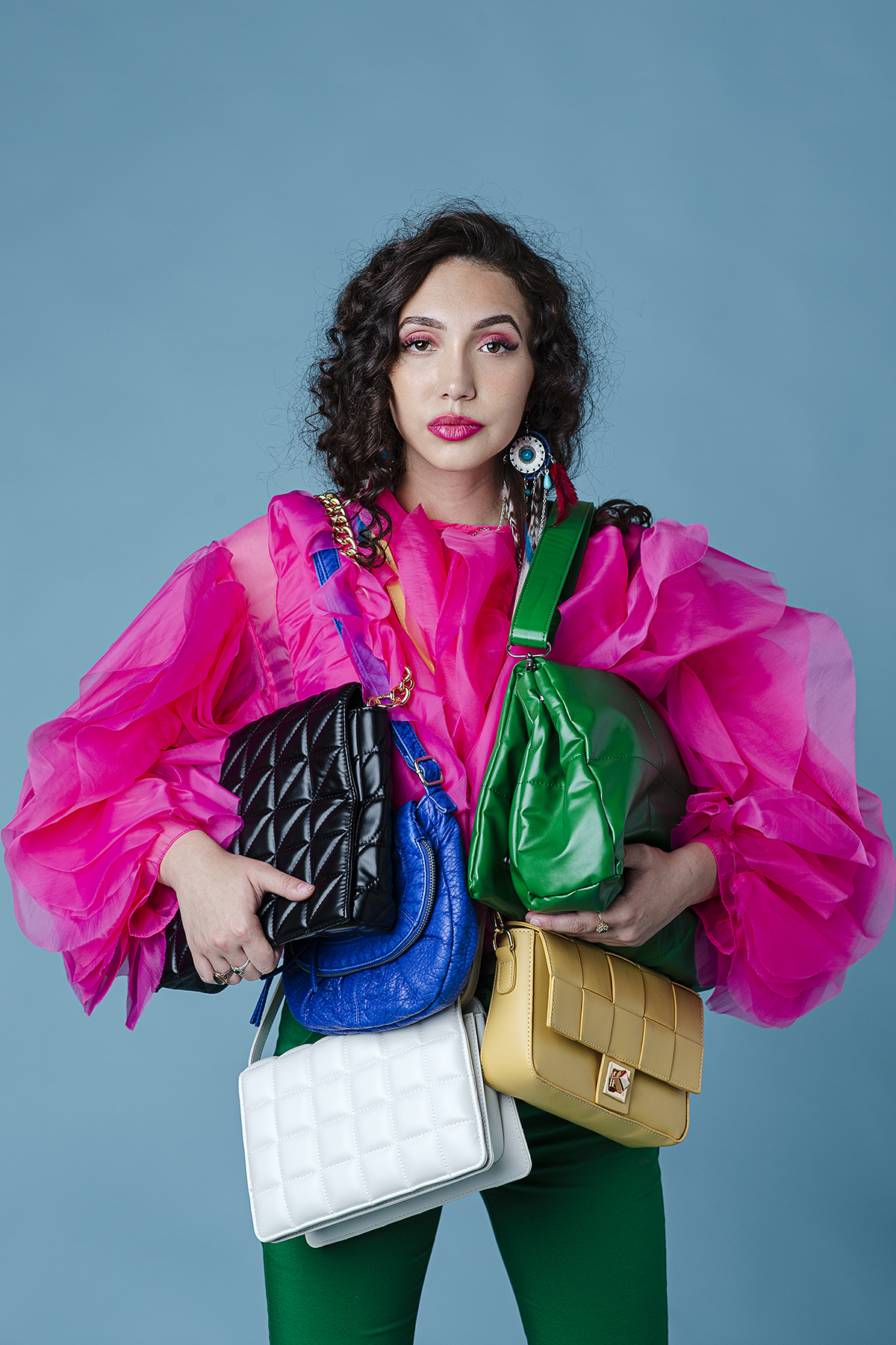 A woman carrying multiple colourful handbags in front of a blue background