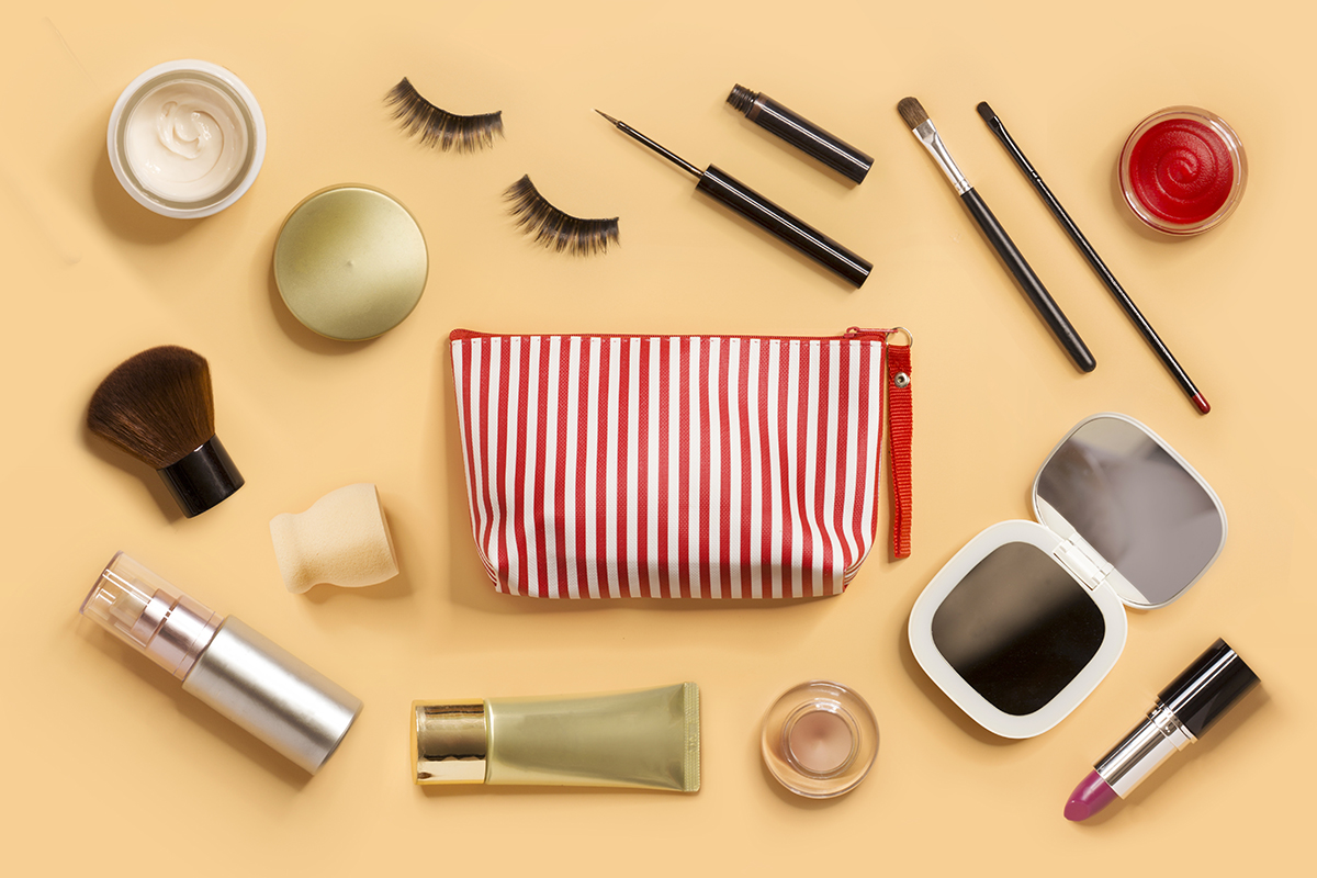 A cosmetic bag surrounded by a range of beauty products on a pale orange background 