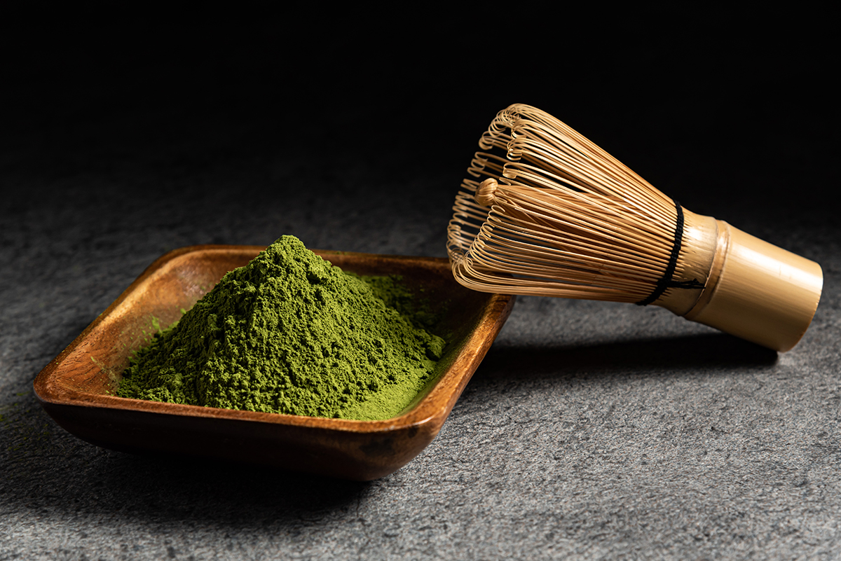A small wooden dish containing matcha powder and a matcha whisk