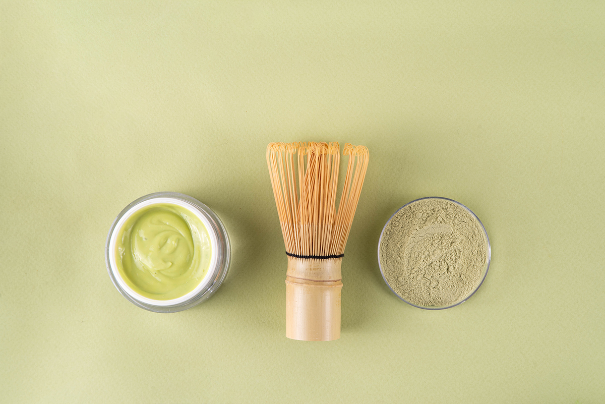 A green-coloured cream, a matcha whisk, and matcha powder on a green background
