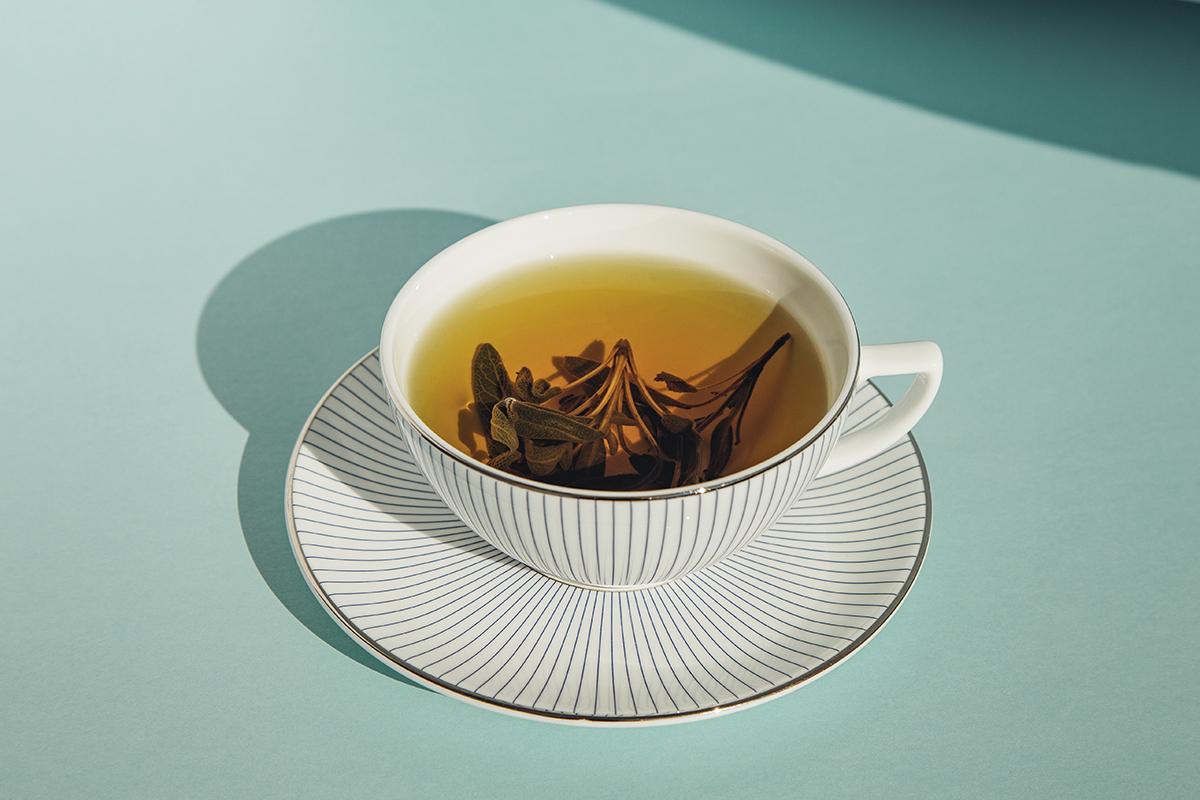 A teacup containing a herbal tea and saucer on a blue background