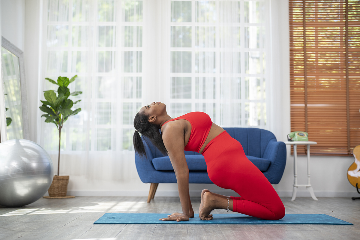 A woman doing a kneeling backbend on a yoga mat in a modern living room