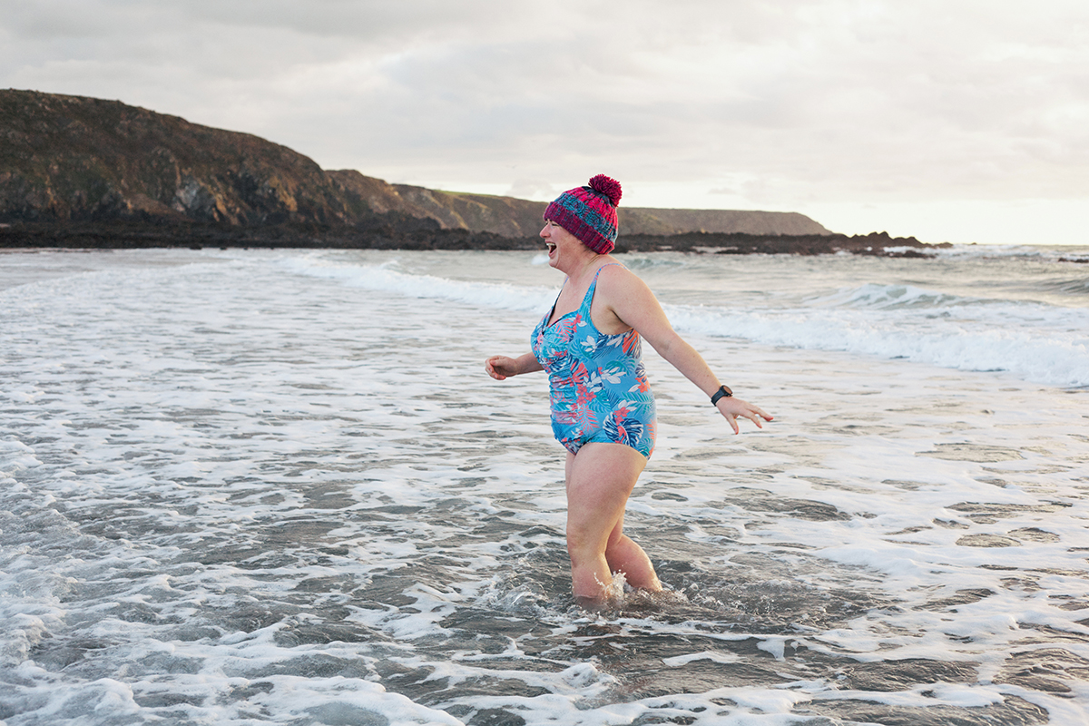 A woman wearing a wooly hat is wading in the sea