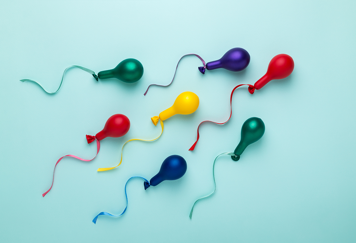 Small colourful balloons with ribbons attached on a blue background to represent sperm