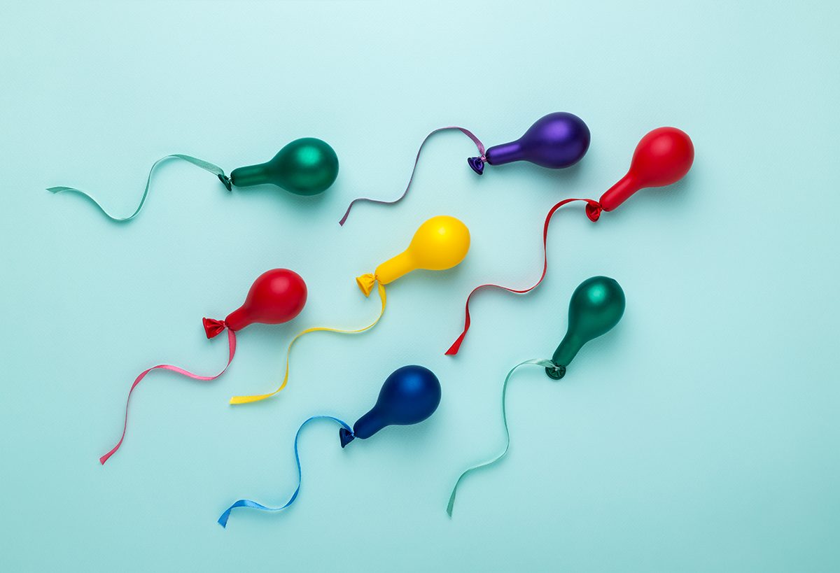Small colourful balloons with ribbons attached on a blue background to represent sperm