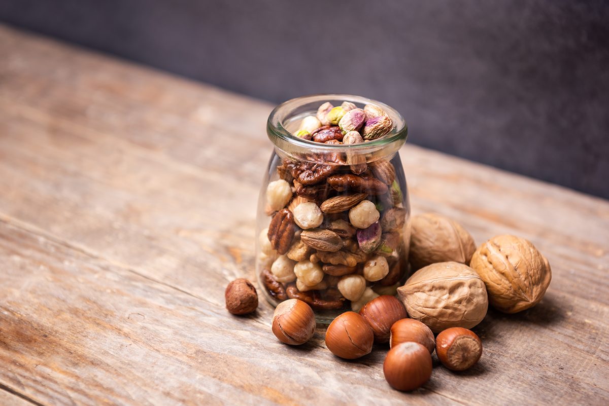 A small glass jar containing a mix of nuts is on a wooden surface.