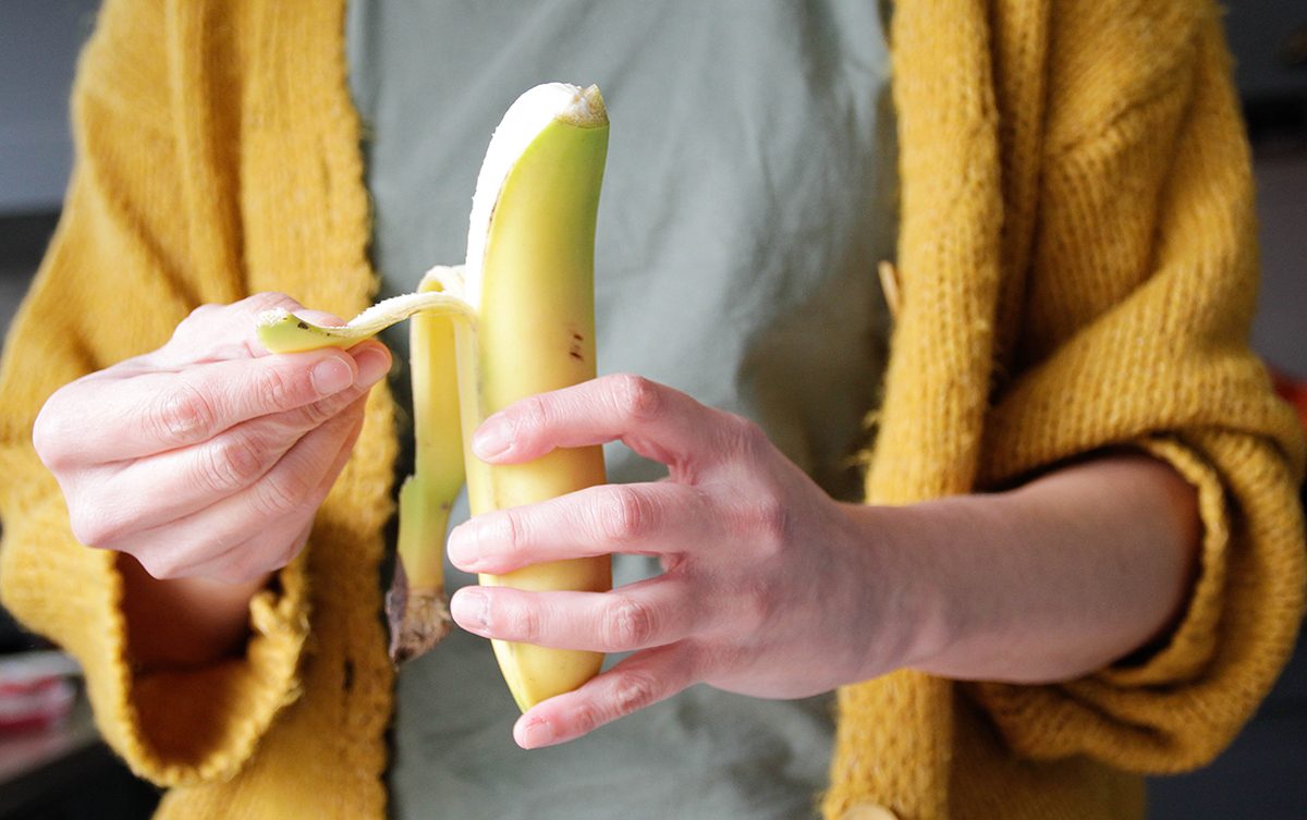 A person wearing a yellow cardigan peels a banana.