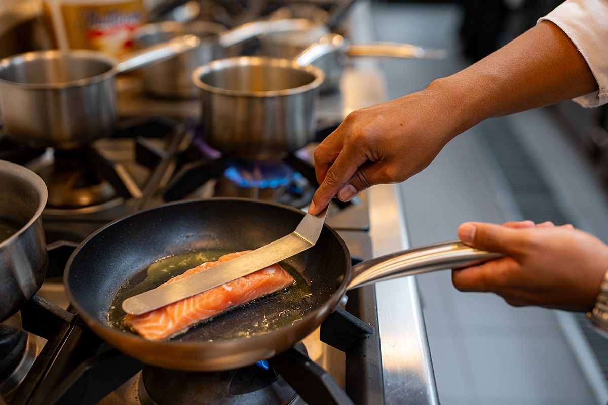 A chef sears a salmon fillet in a frying pan.