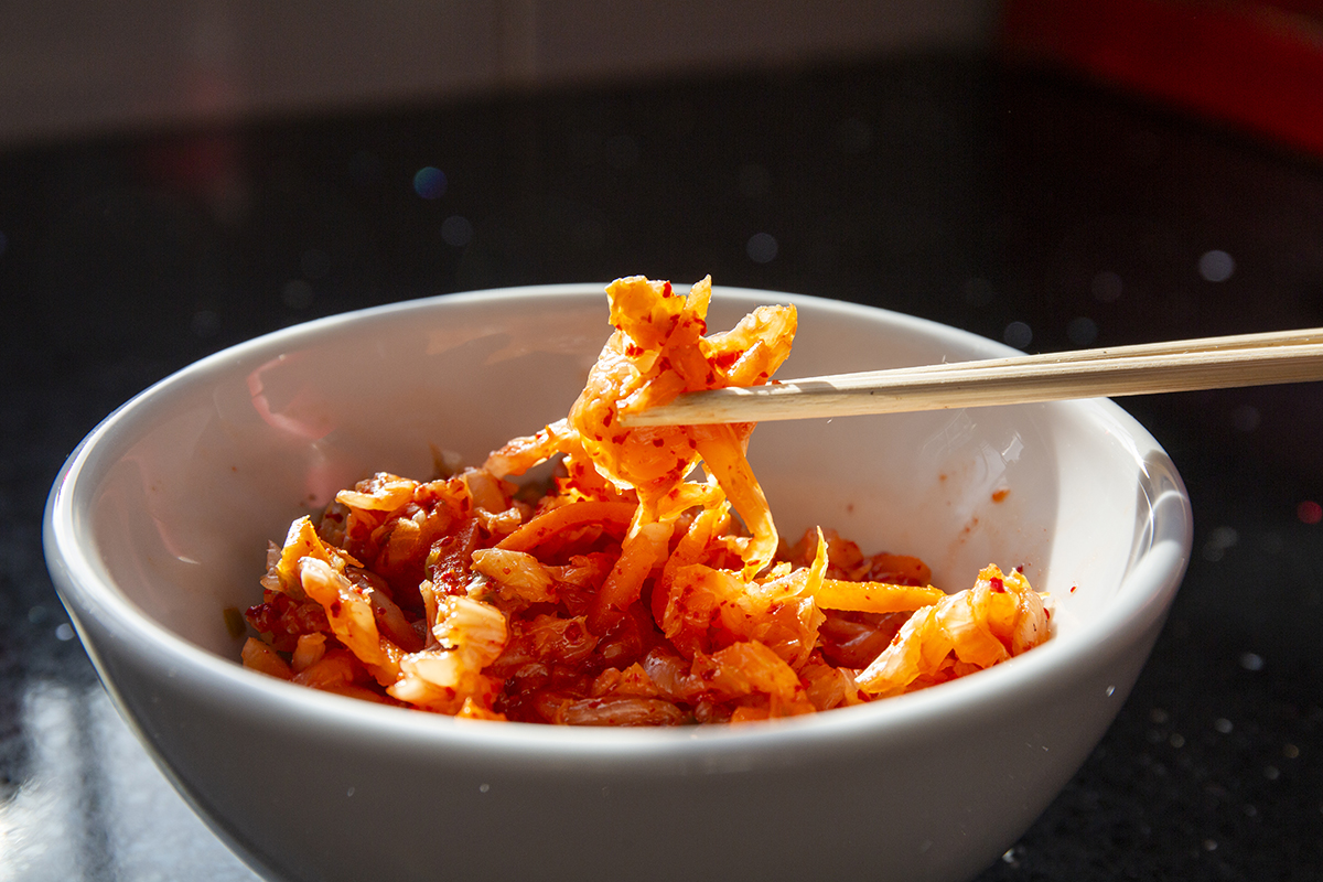 Chopsticks lift a small amount of kimchi from a white bowl.