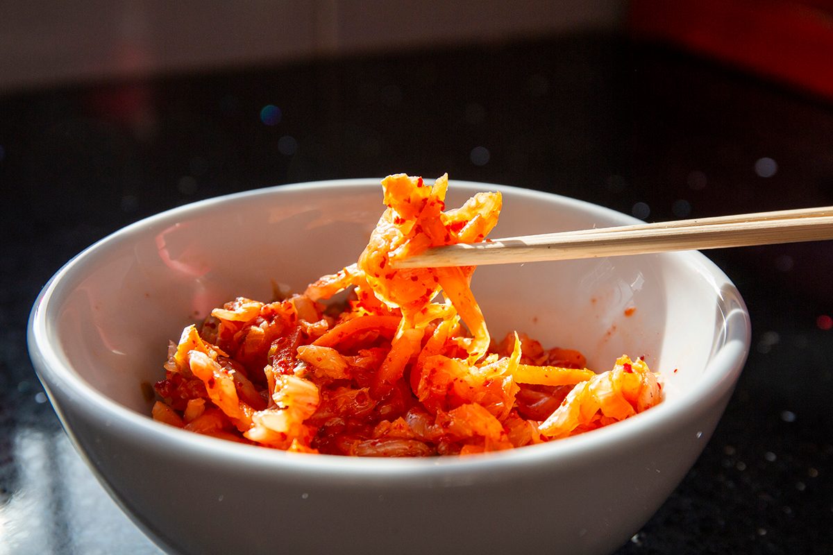 Chopsticks lift a small amount of kimchi from a white bowl.