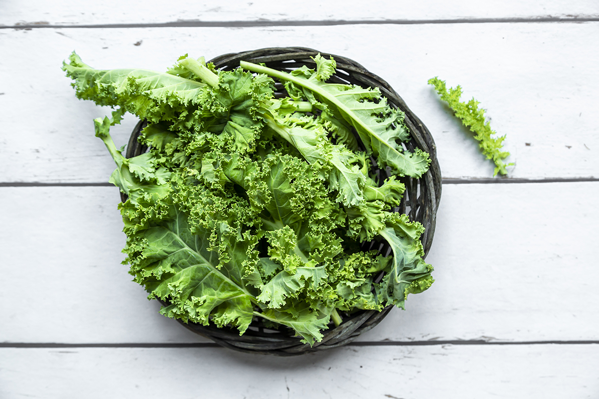 A small basket containing kale is on a white wooden surface.