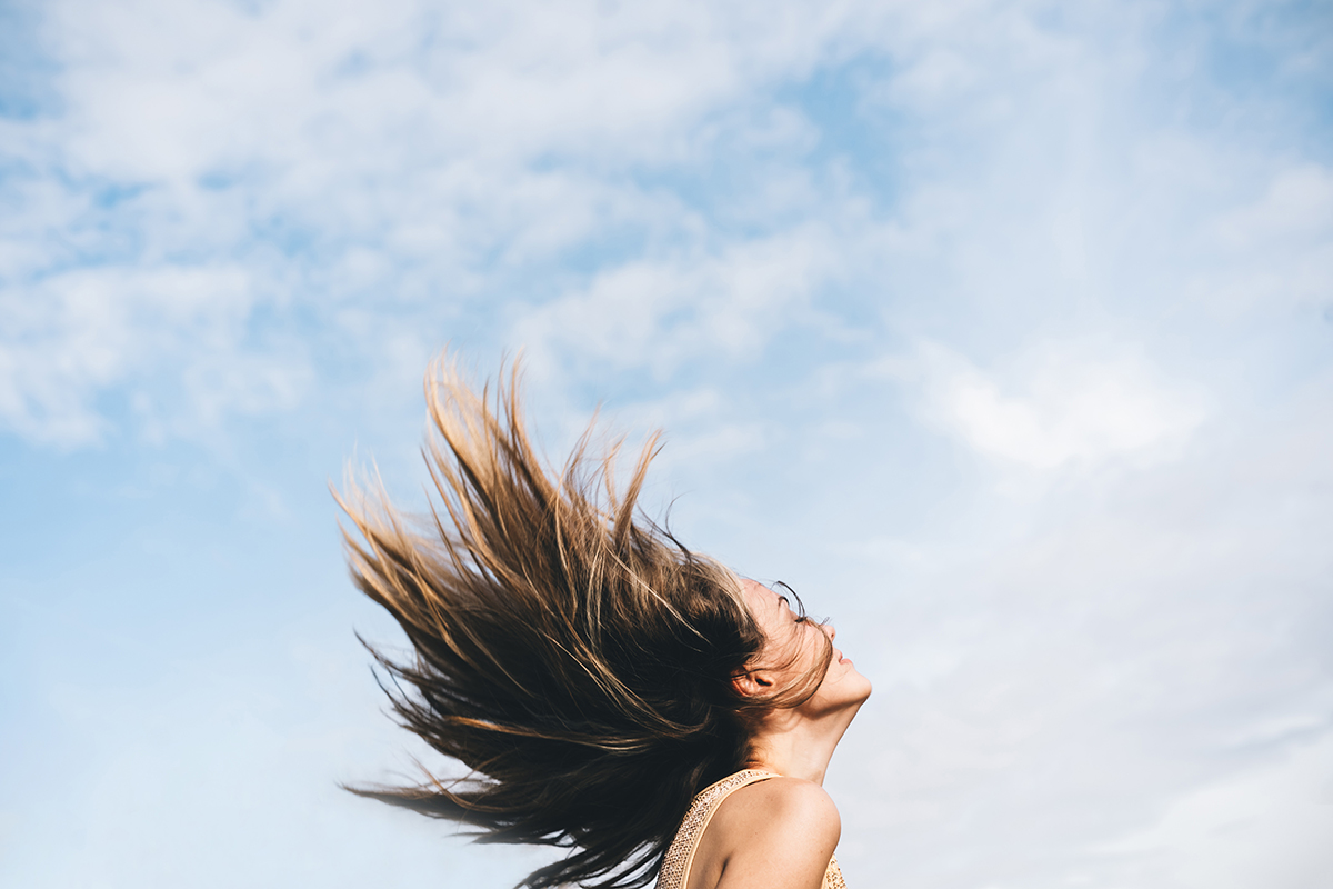 A woman whipping her hair against a cloudy blue sky