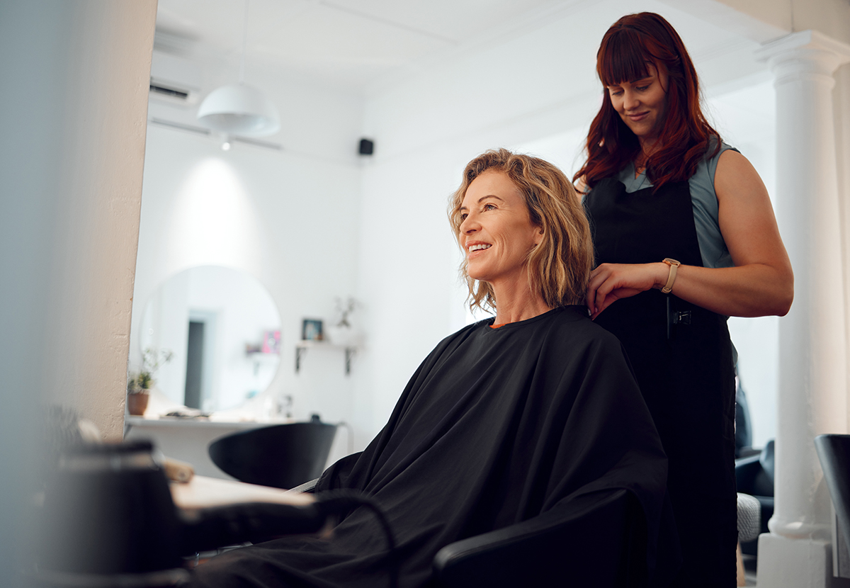 A woman is sitting in a salon chair and getting a haircut