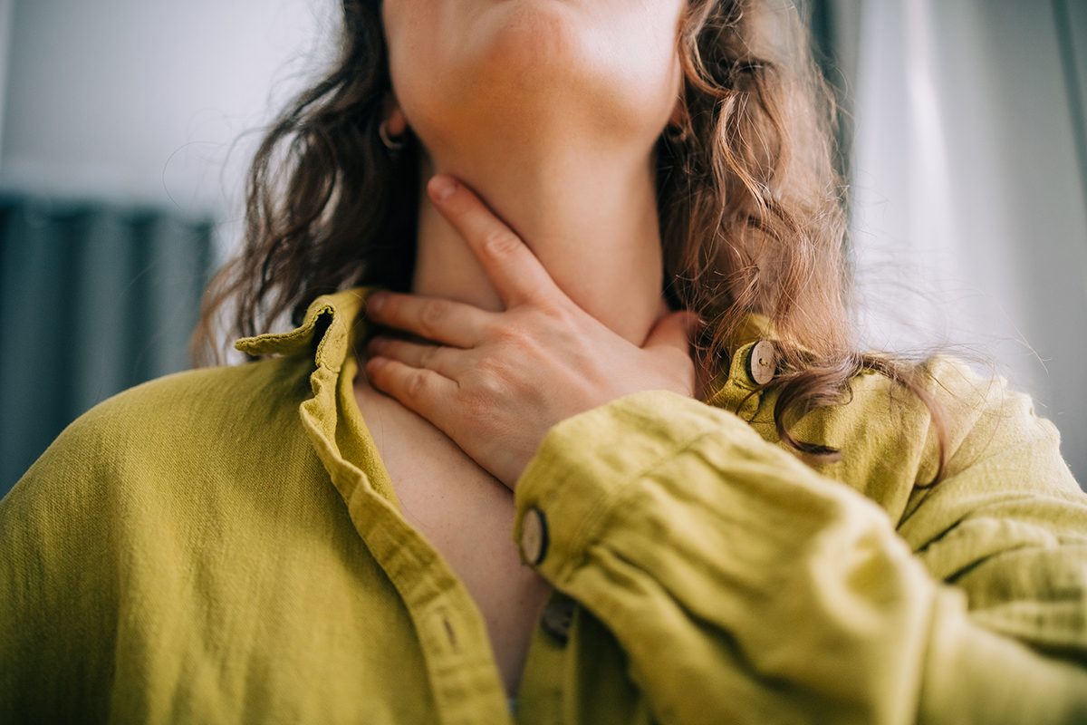 A woman holding neck, suggesting that she's suffering from a sore throat