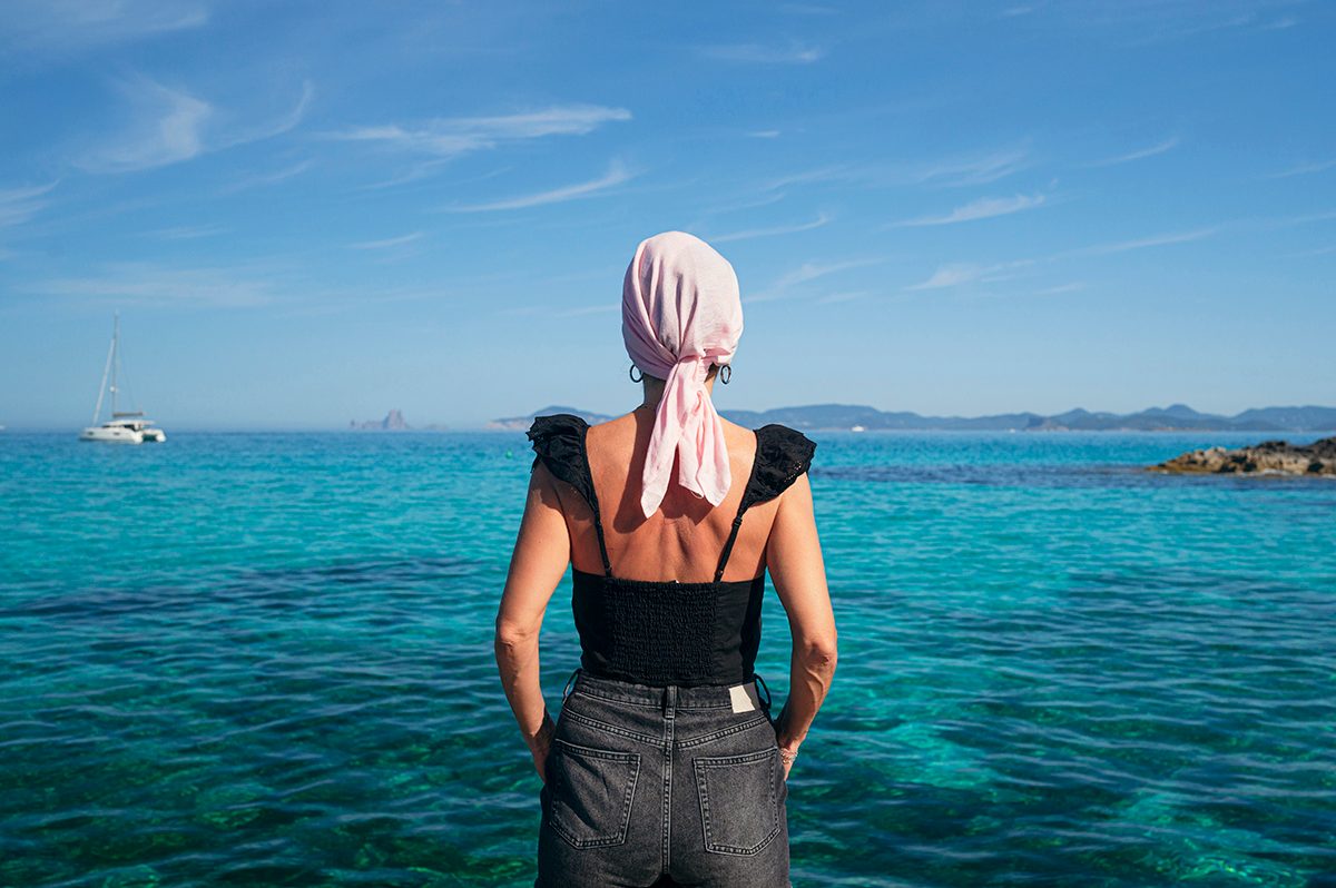 A woman wearing a pink headscarf looks out at a clear blue sea