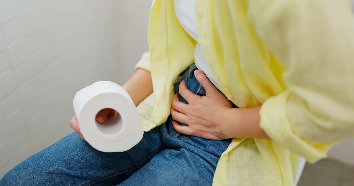 A woman holding her abdomen and a toilet roll, suggesting stomach issues