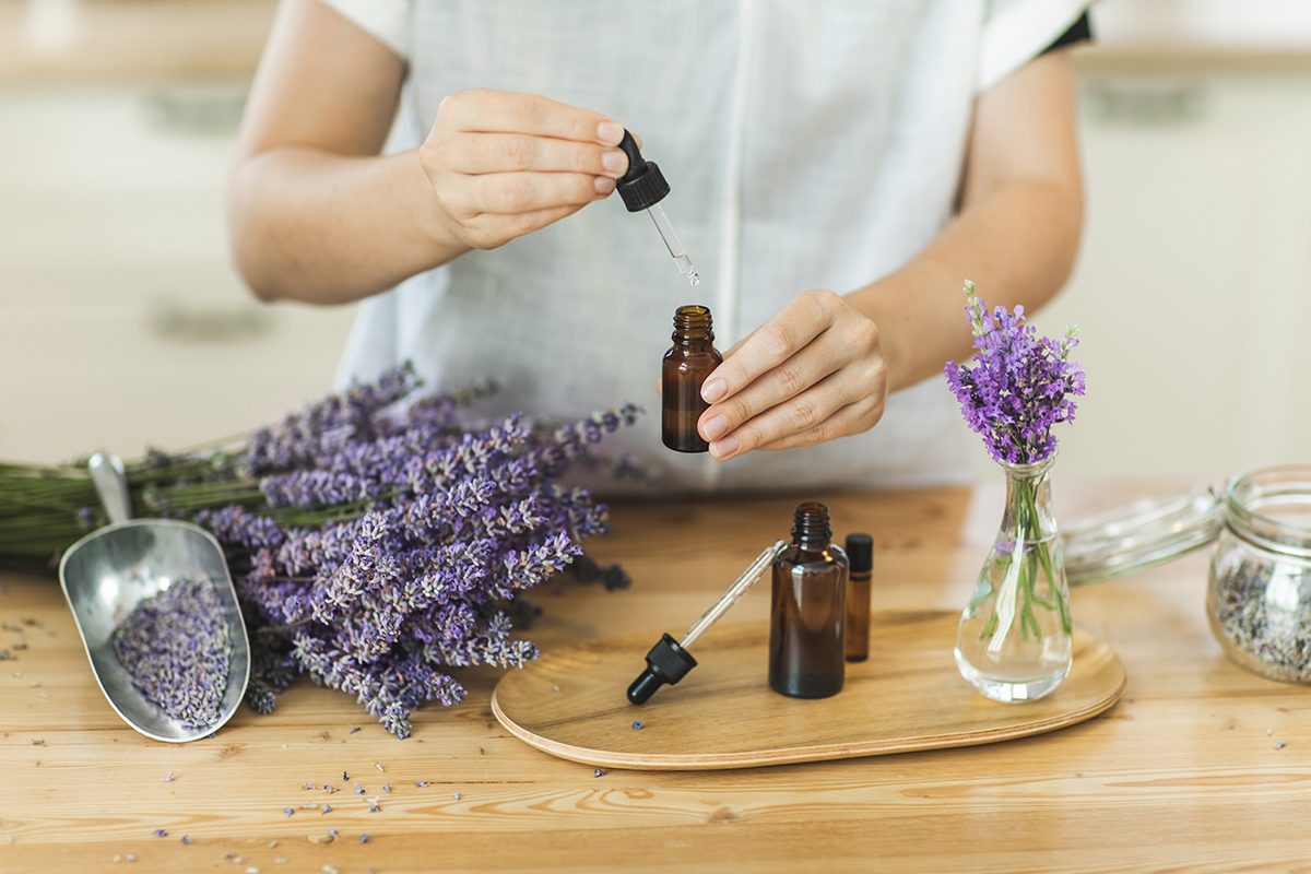 A woman holds a pipette bottle containing lavender oil next to a bunch of dried lavender