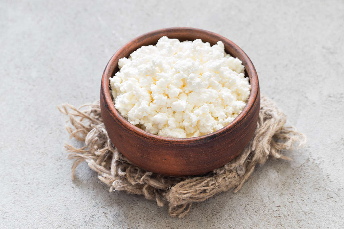 A small clay bowl containing cottage cheese is set on a linen napkin.