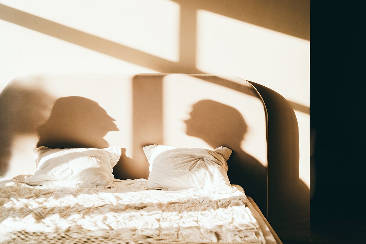 A bed with the shadow of a couple cast across the headboard