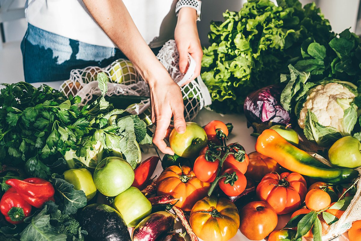 A woman putting fresh fruit and vegetables in a mesh bag at a greengrocers