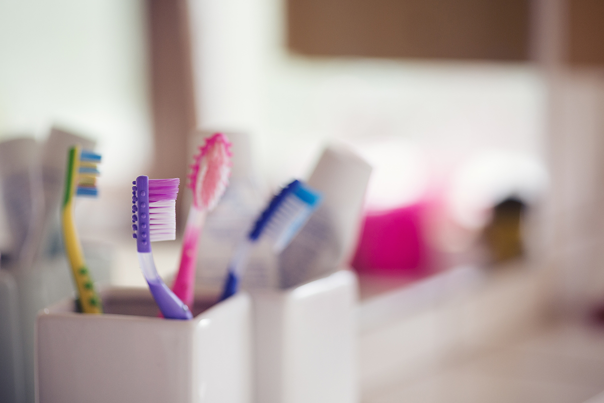 Colourful toothbrushes in a white ceramic toothbrush holder with a blurred background of a bathroom.