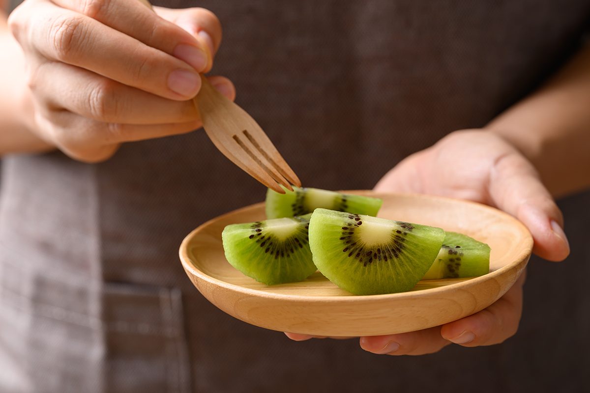 A person eating sliced kiwi fruit from a wooden plate
