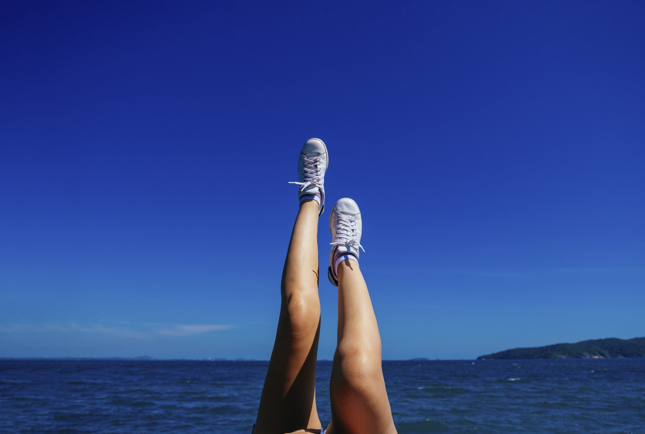 Close-Up Of Woman's Legs Wearing Shoes Against Blue Sky