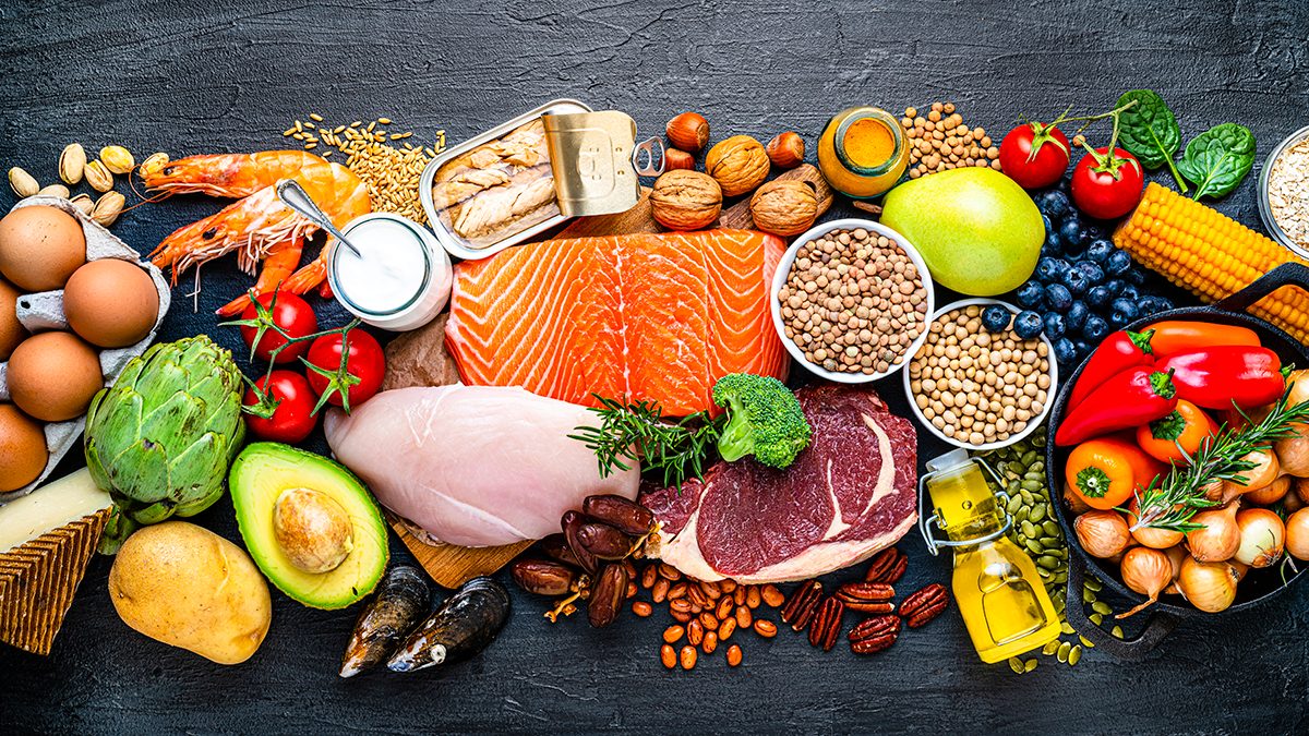 A range of healthy foods, including raw meat, fruits, vegetables, eggs, nuts, legumes and yoghurt