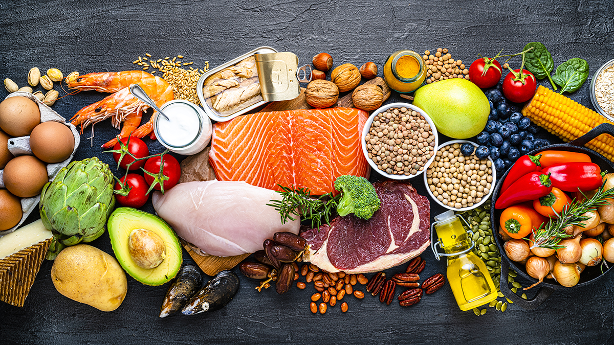 A range of healthy foods, including raw meat, fruits, vegetables, eggs, nuts, legumes and yoghurt