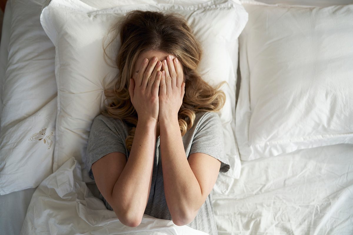 A woman lies in bed covering her face with her hands