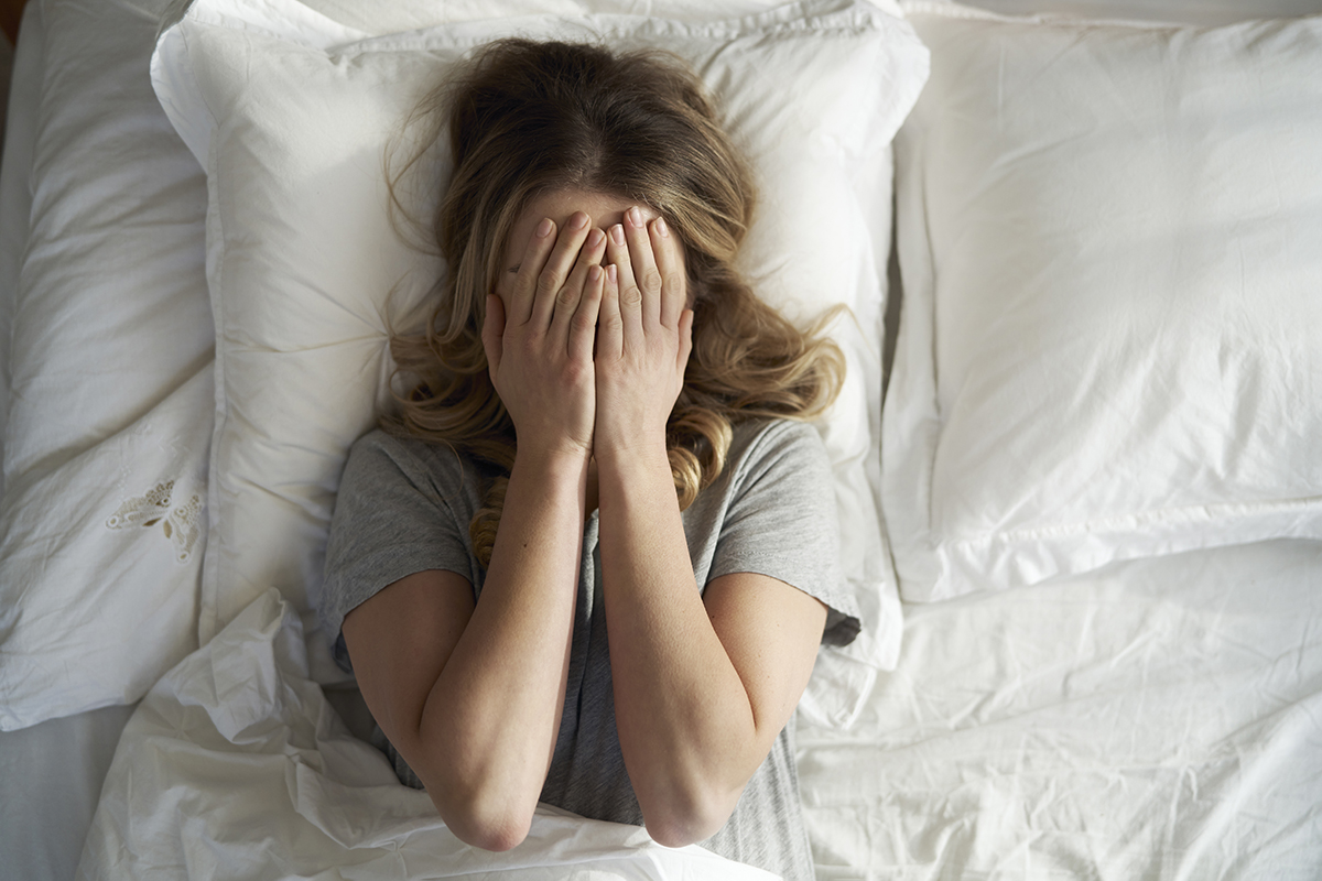 A woman lies in bed covering her face with her hands