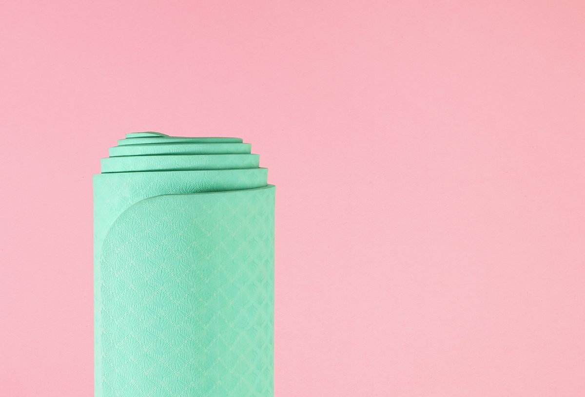 A rolled up green yoga mat against a pink background