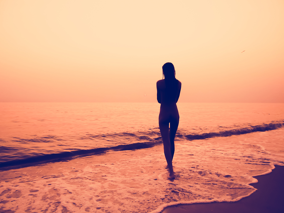 A silhouette of a woman walking in shallow water on a beach