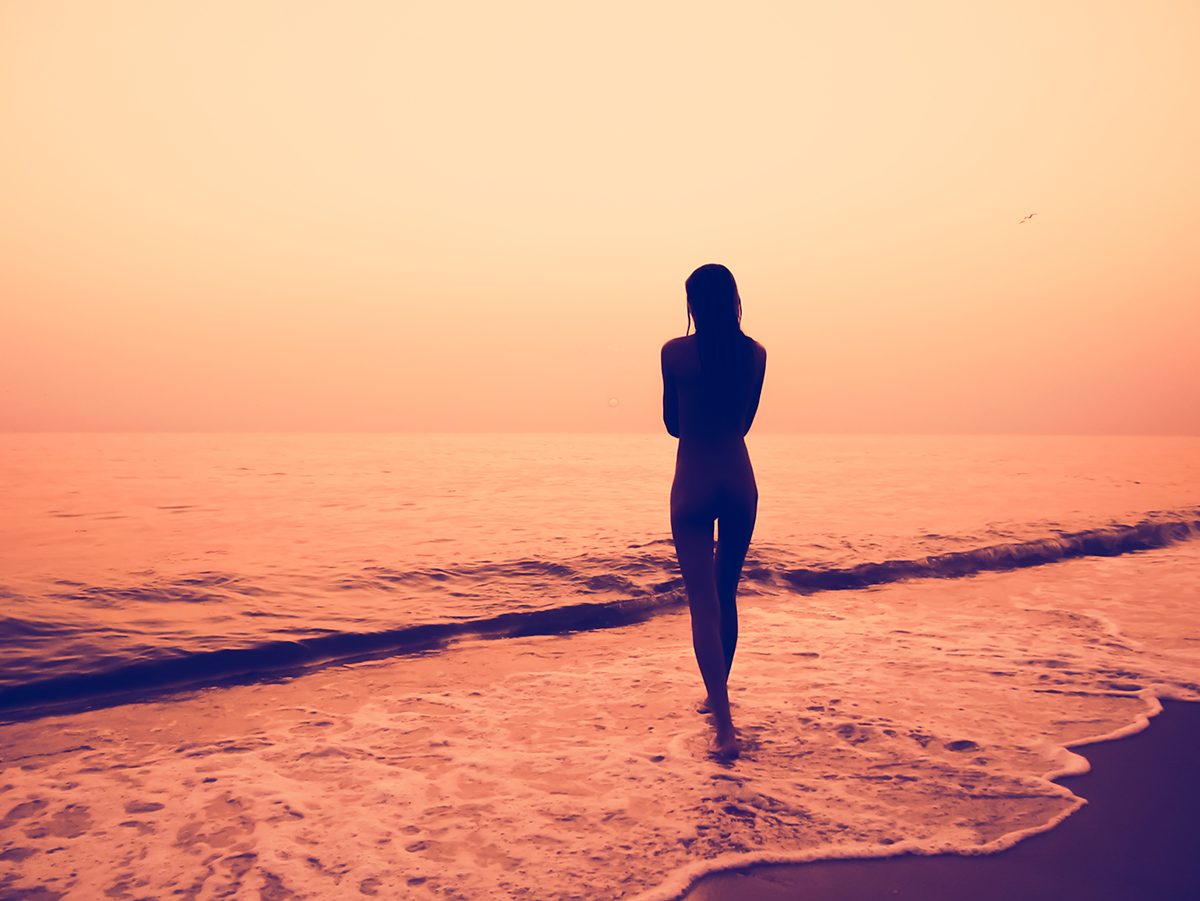 A silhouette of a woman walking in shallow water on a beach