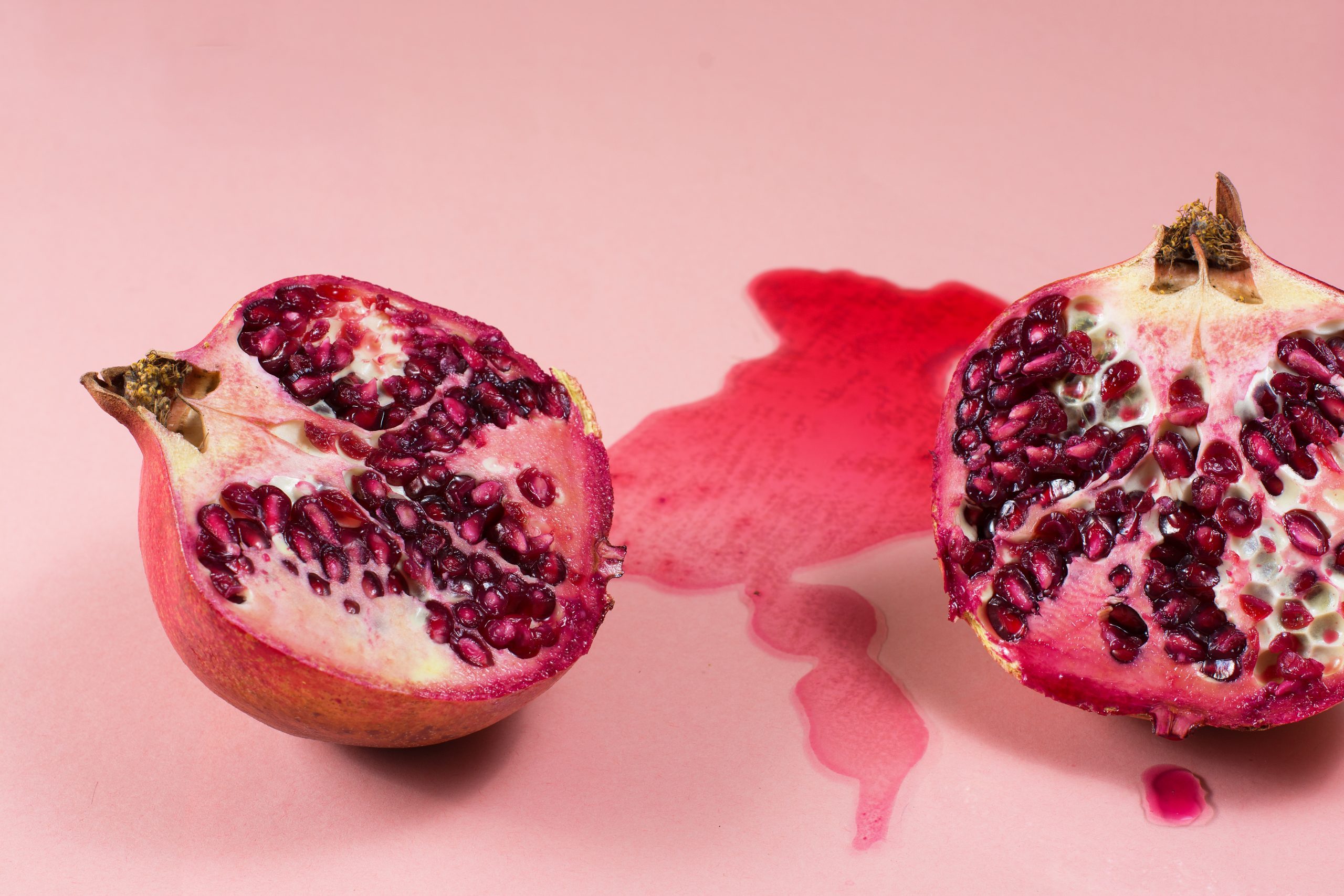 Fresh tasty pomegranate cut into halves. Juice leaked out on a pink background.