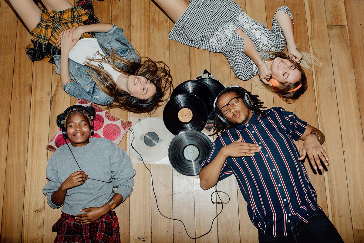 A group of friends lying on the floor listening to music through headphones, surrounded by vinyl records