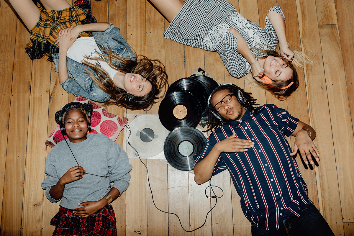 A group of friends lying on the floor listening to music through headphones, surrounded by vinyl records