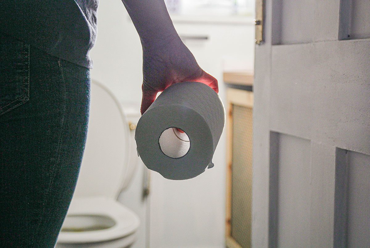 A woman is walking into a bathroom holding a toilet roll
